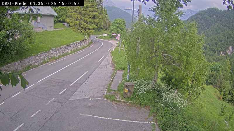 Trenutna slika s cestne kamere v Logu pod Mangartom – pogled na mokro cesto in alpsko pokrajino v živo